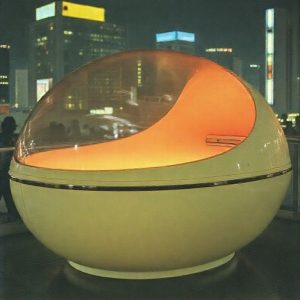 A historical photo of the Sanyo Ultrasonic Bath prototype from the World Expo 1970 Osaka, showing its retro-futuristic egg-shaped design, contrasted with modern Japanese city lights in the background.