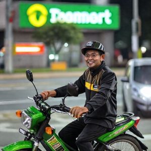Seorang pria tersenyum sambil mengendarai sepeda listrik baru keluar dari gerbang Transmart.
