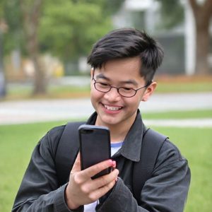 Seorang remaja sedang tersenyum sambil menggunakan aplikasi TikTok di ponselnya, dengan fokus pada pengaturan preferensi konten AI.