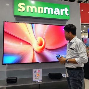 Tumpukan Smart TV 43 inci dengan label diskon besar di area elektronik Transmart, dikelilingi oleh antrean pembeli yang memegang kartu Bank Mega dan ponsel dengan aplikasi Allo Paylater. Suasana toko ramai tapi tertib.